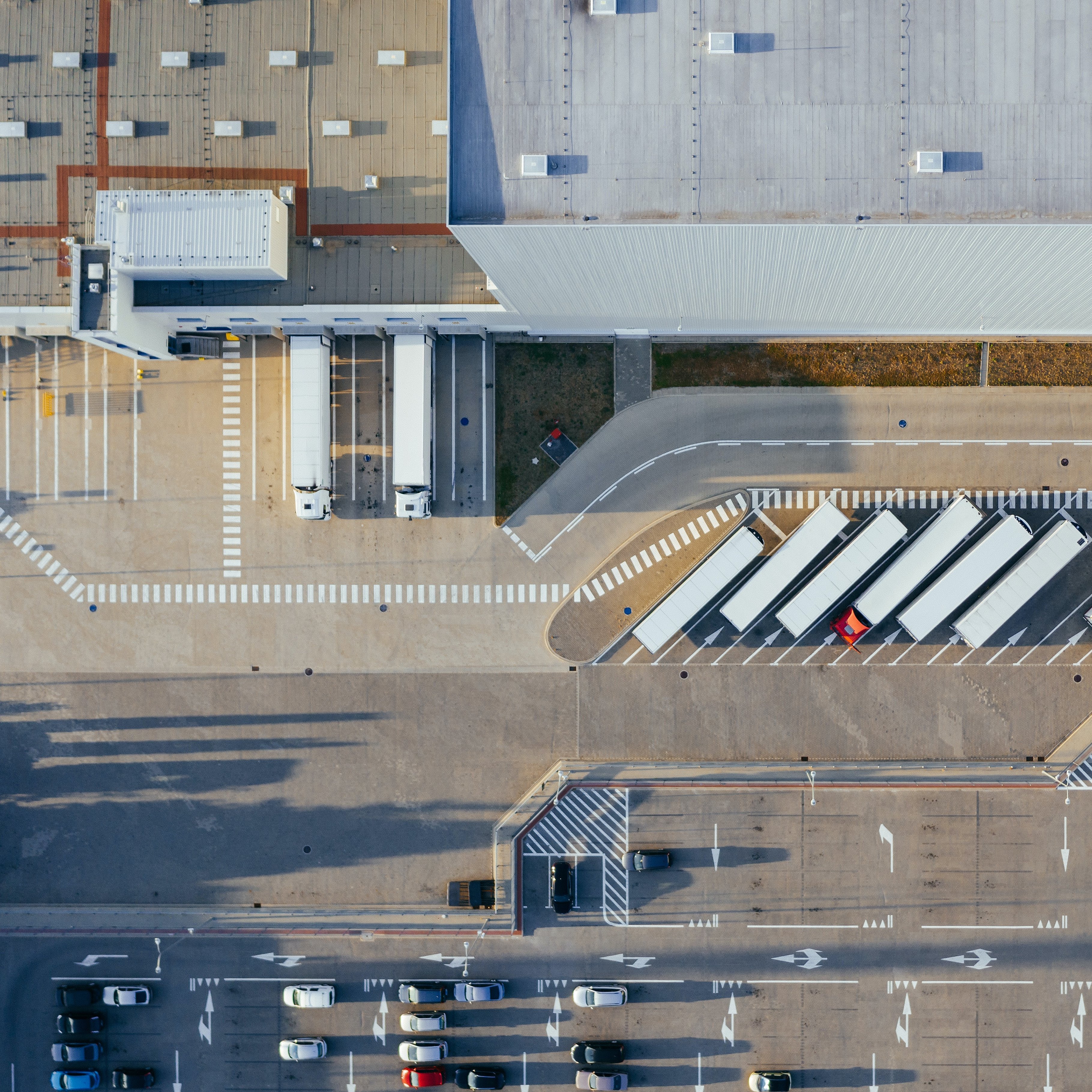 Logistikanlage aus der Vogelperspektive, LKW-Flotte und Logistikhalle sind zu sehen.