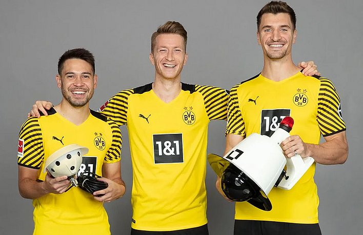 Three Borussia Dortmund players dressed in yellow jerseys hold cameras from Staige.