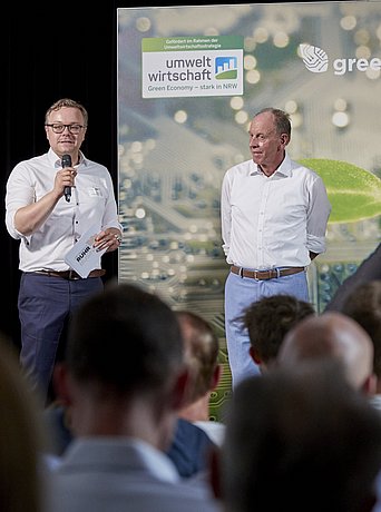 BMR-Geschäftsführer Jörg Kemna und Bottrops OB Bernd Tischler stehen zusammen mit einer Moderatorin auf einer Bühne und führen ein Gespräch.