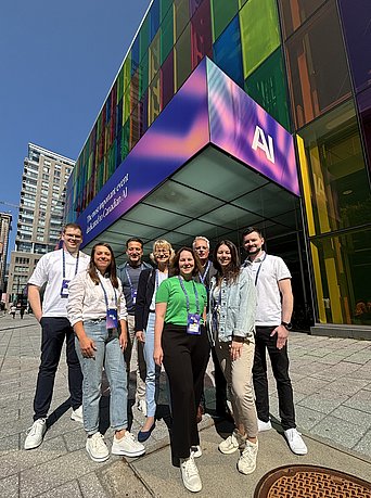 Eine Gruppe aus Männern und Frauen posiert für ein Gruppenfoto vor einem Gebäude.